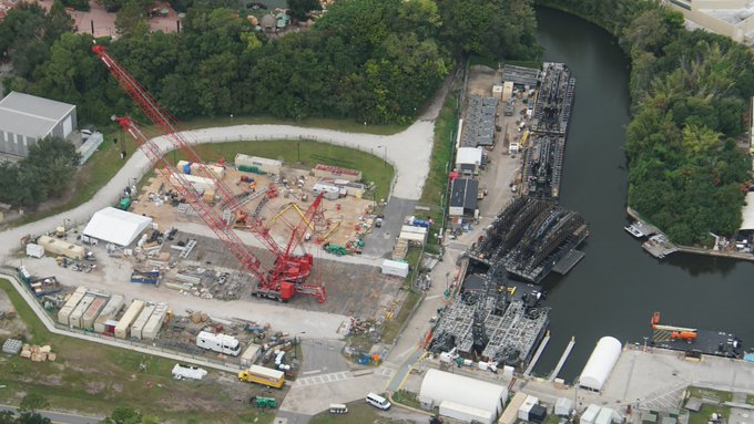 Aerial view of EPCOT’s waterfront construction zone, featuring cranes and equipment as new attractions rise along the lagoon—echoing the transformation for HarmonioUS amid lush greenery.