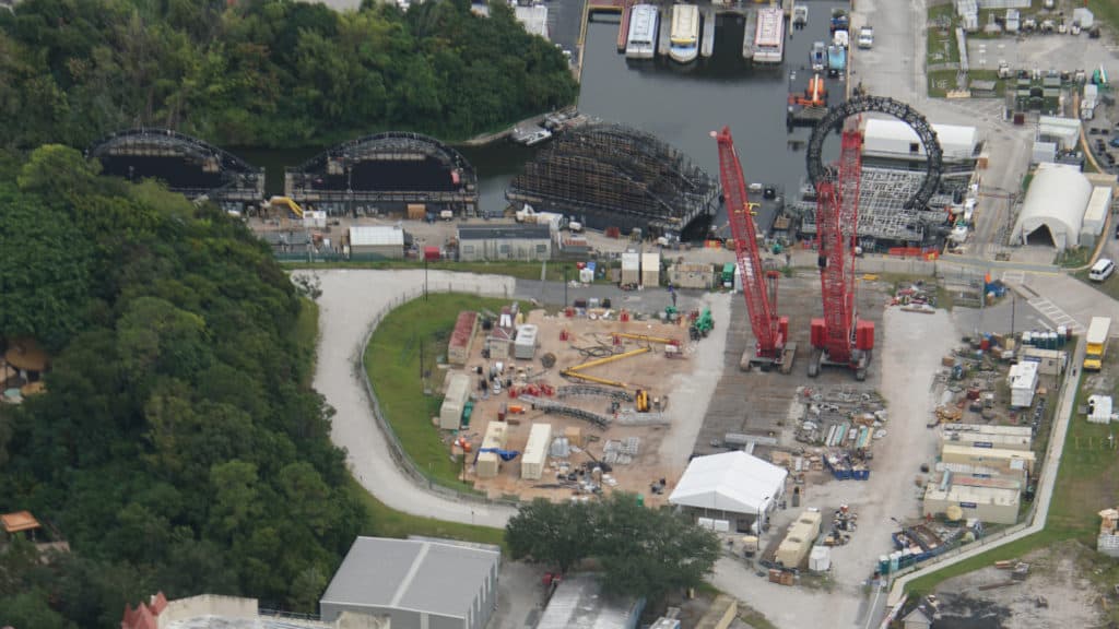 Aerial view of EPCOT’s transformation for HarmonioUS, showcasing active construction with cranes and scaffolding near lush landscaping and shimmering water within the park.
