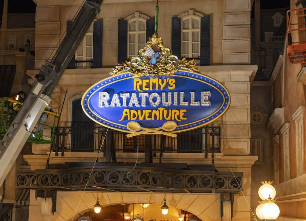 The vibrant blue and gold "Remy's Ratatouille Adventure" sign welcomes fans above the attraction’s entrance at EPCOT, glowing with anticipation as guests eagerly await the long-awaited opening of this charming new addition to the park.