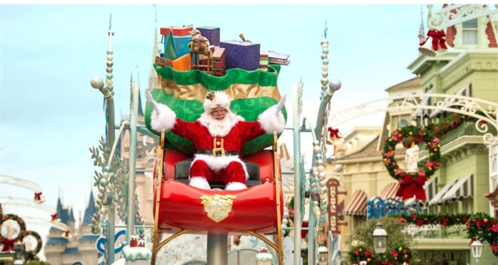 Santa Claus greets guests from a brilliantly decorated red sleigh float surrounded by gifts, gliding down Main Street U.S.A. during the magical Christmas Cavalcade at Magic Kingdom.