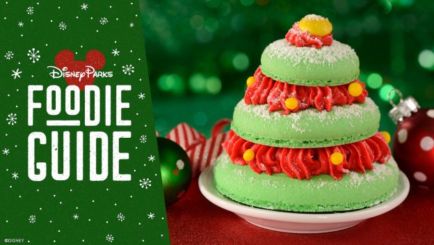 Festive green Christmas tree macaron topped with red frosting and yellow candy, showcased next to the "Disney Parks Foodie Guide"—a magical holiday treat available at Magic Kingdom for Disney fans and foodies to enjoy.