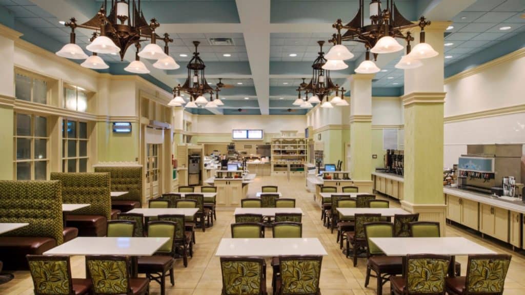 Inviting cafeteria at Disney’s Grand Floridian Resort, featuring green chairs, crisp white tables, and stylish hanging lights, with food counters lining the back—an ideal spot to unwind and recharge during your Disney resort adventure.