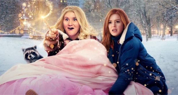 Two costumed characters from Disney+’s “Godmothered” bring winter magic to life, with one joyfully waving her wand and a raccoon character nestled in cozy blankets, surrounded by sparkling lights—capturing the whimsical spirit and movie magic theme park fans love.