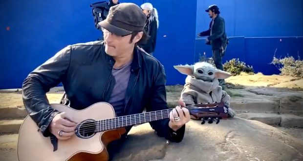 A musician entertains guests alongside Grogu (Baby Yoda) outdoors, with fans and a blue screen backdrop creating a Star Wars-themed experience.