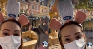 A guest sporting a chef hat Disney ear headband and face mask strikes a fun pose by Remy the rat at the Remy's Ratatouille Adventure fountain, offering fans an exciting first look at this new EPCOT attraction.