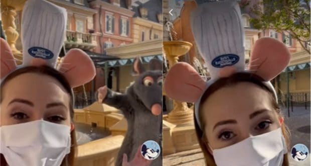 A guest sporting a chef hat Disney ear headband and face mask strikes a fun pose by Remy the rat at the Remy's Ratatouille Adventure fountain, offering fans an exciting first look at this new EPCOT attraction.