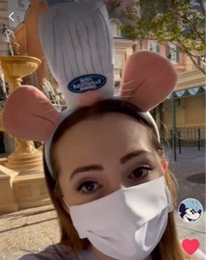 Remy-inspired fan wearing a white face mask and chef hat ear headband enjoys the lively atmosphere of Epcot’s France Pavilion, near the fountain, for an exclusive preview of Remy’s Ratatouille Adventure.