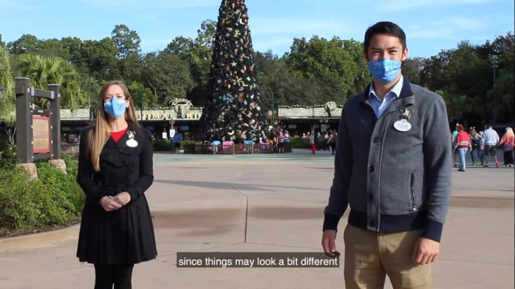 Guests in festive masks gather by a sparkling Christmas tree at Walt Disney World, while Park Hoppers and Disney Ambassadors roam the background, filling Main Street with holiday magic and seasonal excitement.