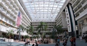 Guests stroll through the bright, open atrium at Orlando International Airport, passing under a massive US flag and palm trees—a first magical sight for theme park visitors arriving in Central Florida.