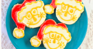 Three Santa-shaped cookies decorated with red hats and yellow icing details rest on a blue plate, capturing the joyful Disney spirit seen throughout the parks—these festive treats are perfect for adding a sprinkle of Disney magic to your holiday celebration.
