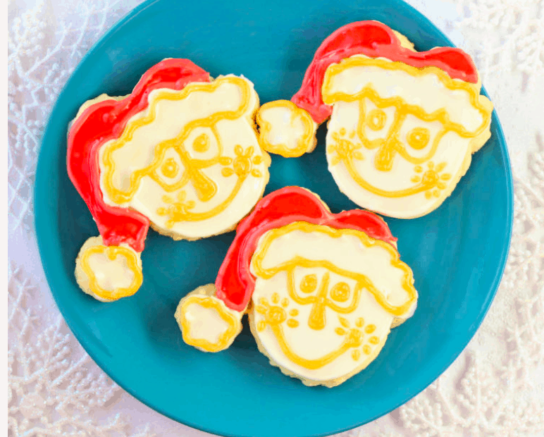 Three Santa-shaped cookies decorated with red hats and yellow icing details rest on a blue plate, capturing the joyful Disney spirit seen throughout the parks—these festive treats are perfect for adding a sprinkle of Disney magic to your holiday celebration.