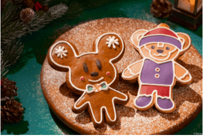 Two festive bear-shaped cookies decorated with Disney flair rest on a round plate dusted with powdered sugar, surrounded by cheerful holiday décor—capturing the whimsical spirit of Disney Parks and perfect for celebrating National Cookie Day or creating magical moments at home.