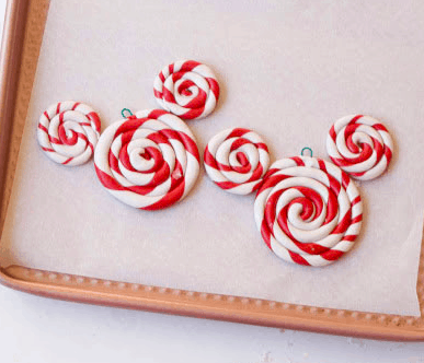 Five red and white swirled peppermint lollipop ornaments shaped like Mickey Mouse are displayed on a baking sheet, ready to add sweet Disney magic to your holiday festivities.