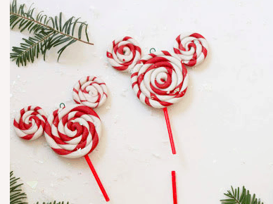 Peppermint swirl lollipops designed like Mickey Mouse heads, set among pine branches on a bright white background—magical holiday treats inspired by Disney parks, perfect for fans dreaming up festive ornament crafts.