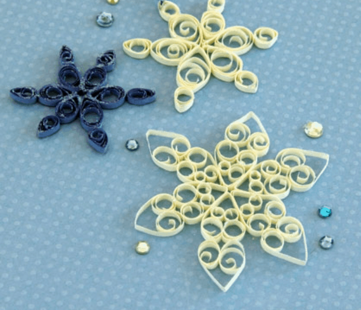 Paper quilled snowflakes inspired by Frozen Fairy Snowflakes and sparkling sequins bring a touch of Arendelle magic to a light blue polka-dotted background, making these decorations perfect for fans creating Disney Parks-inspired crafts.