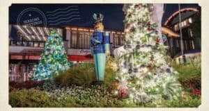 Downtown Disney sparkles with Christmas lights as towering trees twinkle beside a classic toy soldier statue and a cheerful "Season's Greetings" sign. The atmosphere buzzes with holiday spirit, surrounded by iconic Disney shops and tasty quick-service dining options perfect for fueling your festive visit.