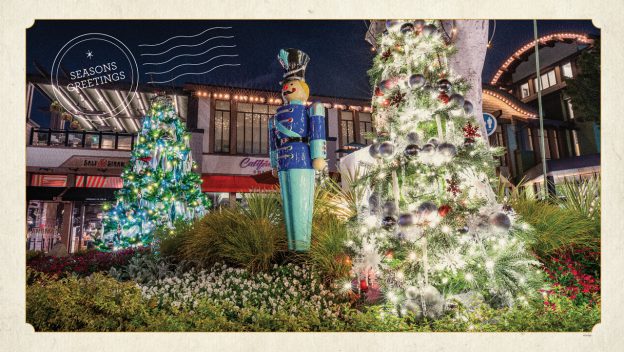 Downtown Disney sparkles with Christmas lights as towering trees twinkle beside a classic toy soldier statue and a cheerful "Season's Greetings" sign. The atmosphere buzzes with holiday spirit, surrounded by iconic Disney shops and tasty quick-service dining options perfect for fueling your festive visit.
