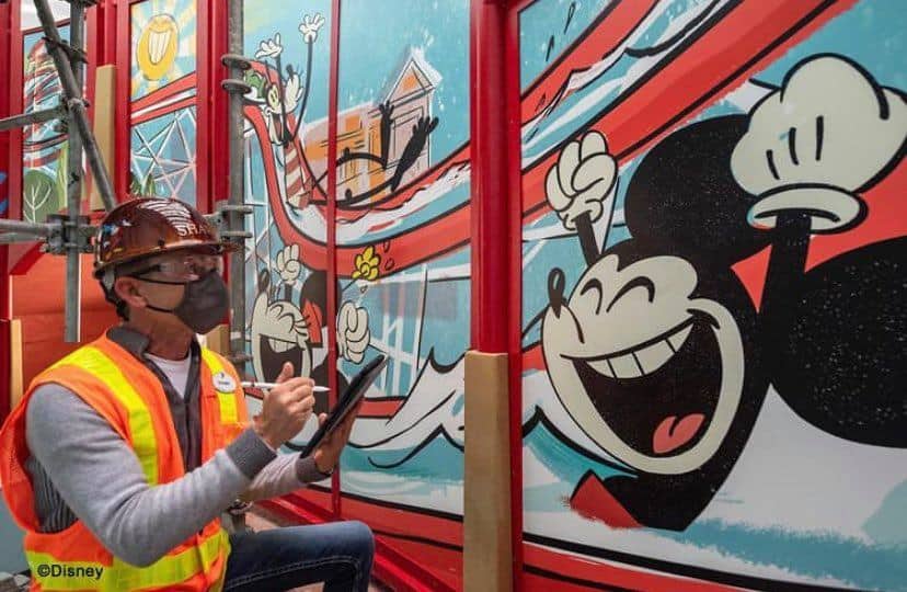 Mickey Mouse comes to life in vibrant colors as a mural is painted on a wall near Disney’s Boardwalk Resort, capturing the fun and festive spirit of the nearby Keister Coaster Pool Slide amidst an active construction backdrop.