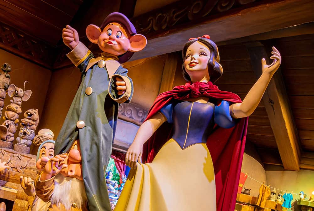 Snow White and Dopey, vibrant as ever, pose together amid the storybook charm of a wooden cottage scene from Disneyland’s Snow White’s Enchanted Wish attraction.