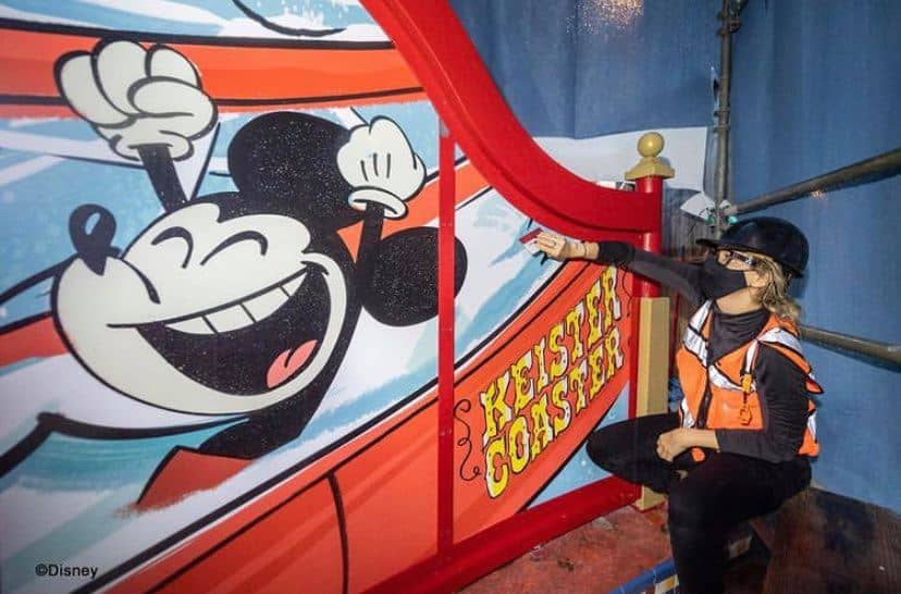 A Boardwalk Resort Cast Member in a safety vest checks out the vibrant Mickey Mouse mural on the iconic “Keister Coaster” slide sign at Disney’s Boardwalk pool.