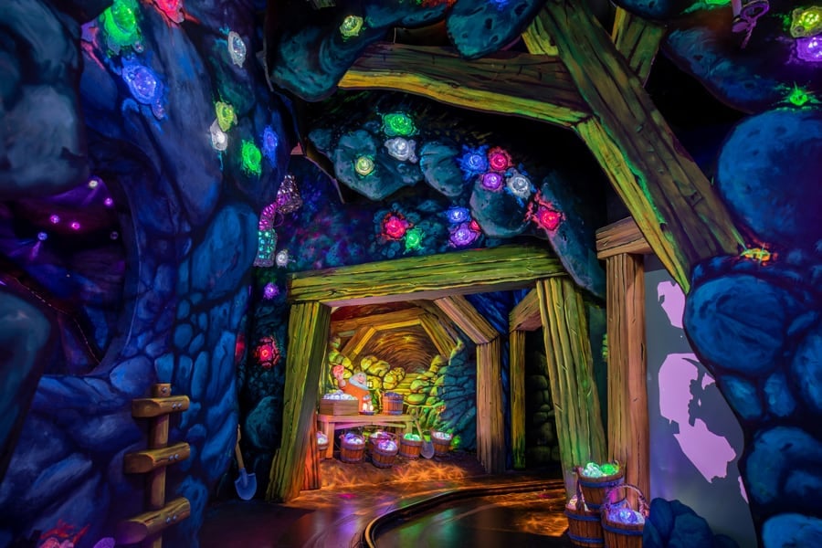 A vibrant mine tunnel sparkling with neon crystals, illuminated in dazzling colors and framed by rustic wooden beams overhead, capturing the enchanting atmosphere of Snow White’s Enchanted Wish attraction at Disneyland.
