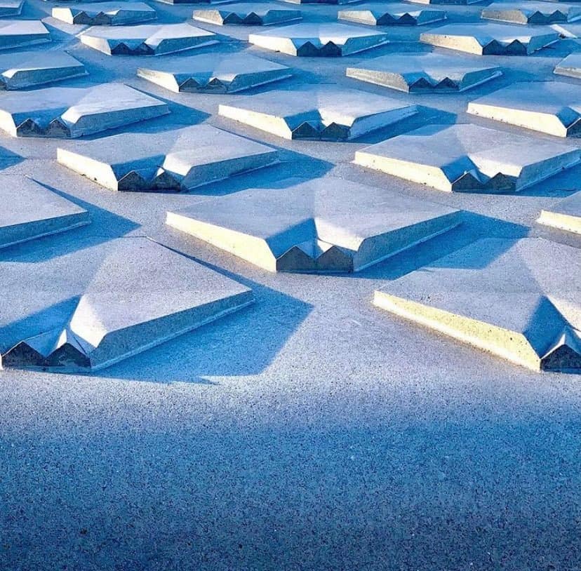 Rows of geometric concrete sculptures cast cool blue shadows across the textured ground, reminiscent of the imaginative style at EPCOT’s Main Entrance Plaza—a signature example of Disney Imagineering.