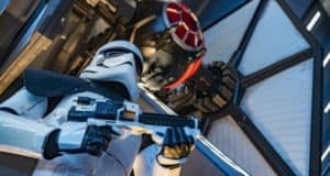 A stormtrooper stands ready with a blaster in front of a TIE fighter inside the Rise of the Resistance attraction’s futuristic hangar, immersing Star Wars fans in the adventure at Disney Parks.