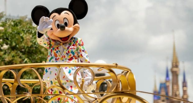 Mickey Mouse dazzles fans in a vibrant confetti suit as he waves from a shimmering gold parade float, celebrating Walt Disney World's phased reopening.
