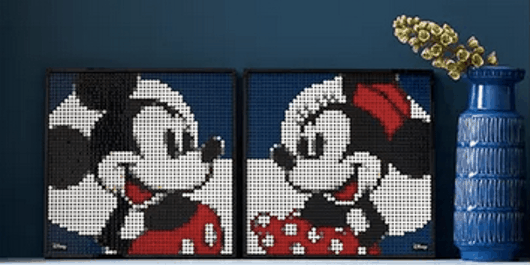 Celebrate Disney magic at home with two framed LEGO Art mosaics featuring Mickey Mouse and Minnie Mouse gazing at each other, beside a cheerful blue vase filled with yellow flowers—perfect for any fan of the theme park experience.
