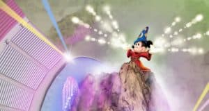 Mickey Mouse, wearing his iconic wizard hat, stands atop a dramatic rocky stage as he conjures dazzling magical lights during the spectacular Fantasmic! nighttime show at Disney World.