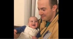 A beaming baby in a white bib gazes up at an adult wearing a tan hoodie, both sharing an infectious laughter that echoes like the joyful sounds down Main Street, filling the space with theme park magic and baby giggles.