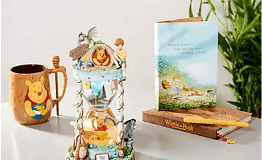 Winnie the Pooh mug, themed hourglass, collectible card, storybook, and pencil displayed on a table with lush greenery in the background—perfect for fans of Disney's Hundred Acre Wood experience.