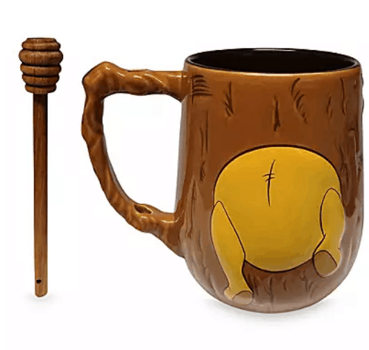 Winnie the Pooh-themed brown mug featuring Pooh Bear’s iconic yellow bottom playfully peeking out, paired with a wooden honey dipper stick—an enchanting souvenir that brings a touch of Hundred Acre Wood magic to your home after your visit to the parks.
