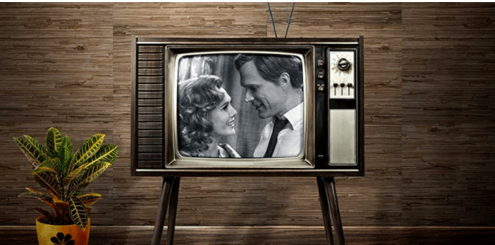 Classic black-and-white scene of Wanda and Vision beaming on an old-fashioned TV, just like in the opening moments of WandaVision at Disney California Adventure’s Avengers Campus; a retro yellow-potted plant props up the set, channeling nostalgic vibes as if getting ready for the show’s iconic era-inspired soundtrack to fill the park.