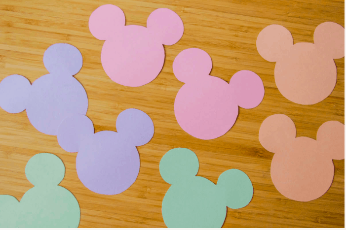 Brightly colored Mickey-shaped paper cutouts scattered across a wooden table, reminiscent of the festive crafts and decor you’d find at Disney parks—ideal for adding magic to your Valentine’s Day treat bags.