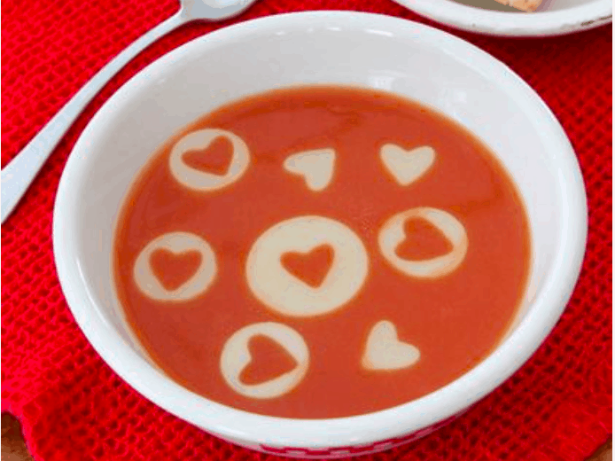 Valentine Soup garnished with cream hearts, served on a red textured cloth—an enchanting treat ideal for sharing magical Disney moments with your Minnie at the parks.