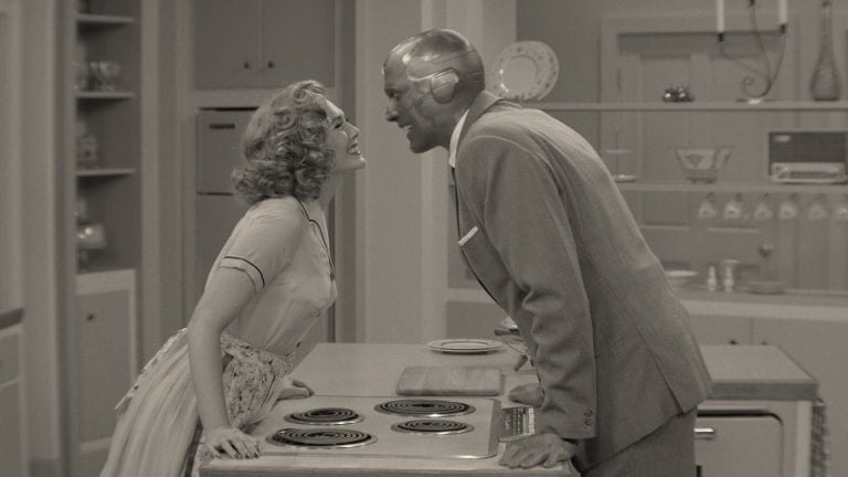 Wanda and Vision share a joyful moment, leaning in with smiles, inside a retro-themed kitchen set straight out of a classic TV sitcom—just like scenes from Marvel’s WandaVision at Avengers Campus or Disney Parks.