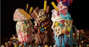 Three over-the-top milkshakes, stacked with candy, cookies, cotton candy, and an entire slice of cake, stand out against a dark backdrop—Disney Springs’ signature Instagrammable treats. A must-try for Disney fans seeking the ultimate sweet fix or families exploring spots where kids can Eat Free in Walt Disney World Resort.