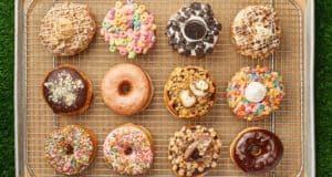 A mouthwatering lineup of twelve whimsical Everglazed Donuts sits on a cooling rack at Disney Springs, each one loaded with playful toppings like rainbow candies and pastries—an Instagram-worthy sweet treat to pair perfectly with Cold Brew during your magical visit.