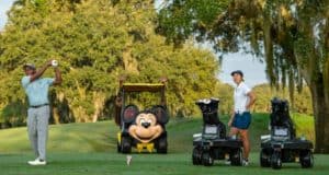At Walt Disney World’s scenic golf course, a guest takes a swing as another enjoys the moment, while a playful golf cart adorned with Mickey Mouse’s smiling face adds classic Disney magic to the fairway experience.