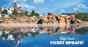 Blizzard Beach water park featuring thrilling slides, rugged rocky hills, lush trees, and a bright blue sky mirrored in the tranquil water. On-screen text announces: "Ticket Update! Discover the latest Blizzard Beach tickets and Disney ticket options for your next adventure.