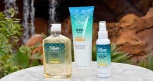 Disney Resort H2O+ bath products are displayed on a marble table outdoors, framed by lush greenery and a waterfall, immersing guests in the signature luxury of Disney Resort experiences—now available for fans to recreate Disney magic at home.