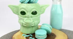A whimsical Yoda mug filled with blue Mando Macarons and a chilled bottle of Blue Milk, all served on a wooden tray—serving up Star Wars treats straight from Galaxy’s Edge.