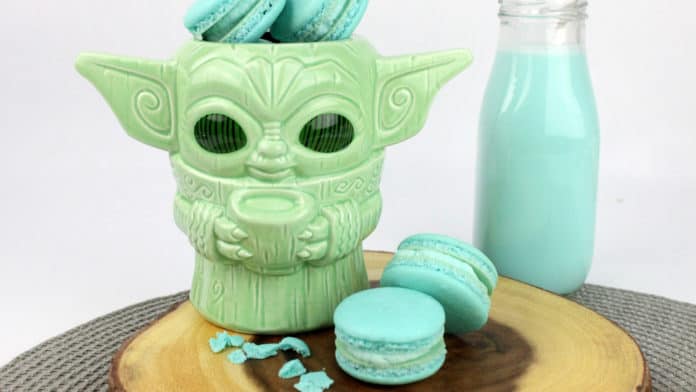 A whimsical Yoda mug filled with blue Mando Macarons and a chilled bottle of Blue Milk, all served on a wooden tray—serving up Star Wars treats straight from Galaxy’s Edge.