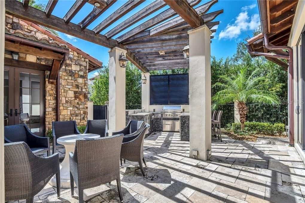 Sun-drenched patio at a Disney Resort Home, complete with wicker lounge chairs, a barbecue grill, and stone flooring beneath swaying palms and a wooden pergola—this magical retreat was recently snapped up for $2.4 million.