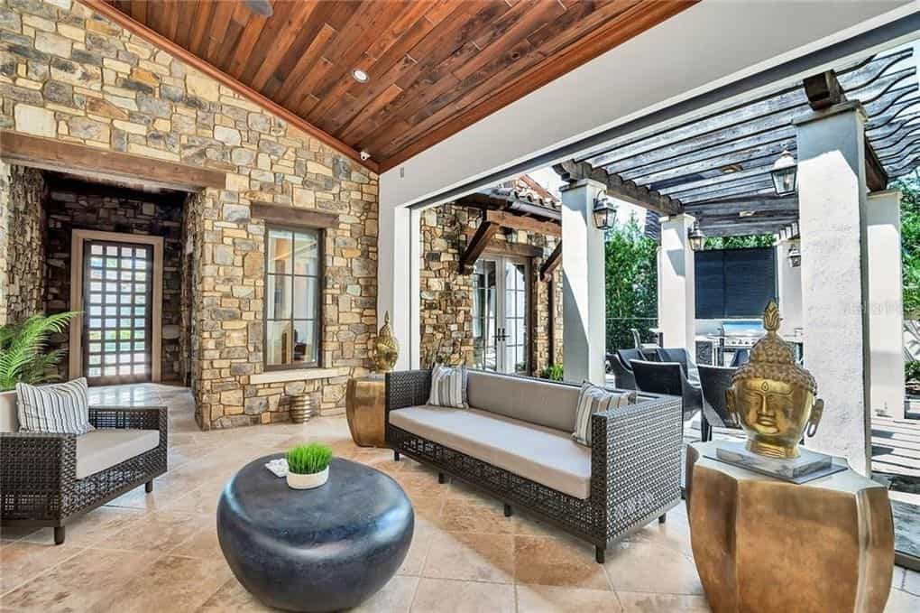 A stylish stone patio evokes the atmosphere of a Disney Resort, complete with plush modern sofas, a sleek black round table, Buddha statues for that signature themed charm, and a wooden pergola above—inviting you to relax in true Disney-inspired luxury right at home.