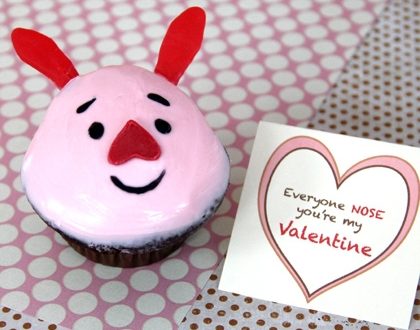 Pink Piglet Cupcake styled with a cheerful pink face, red heart-shaped nose, and matching ears sits by a Valentine card edged in hearts—this whimsical treat from our Valentine’s Day bakery collection brings sweet theme park fun straight to your celebration.