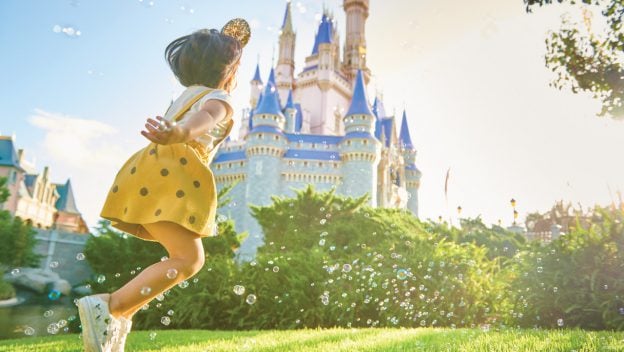 A child in a bright yellow dress dashes toward Cinderella Castle at Walt Disney World, surrounded by sparkling bubbles, evoking the enchanting atmosphere guests experience with a Discover Disney Ticket.