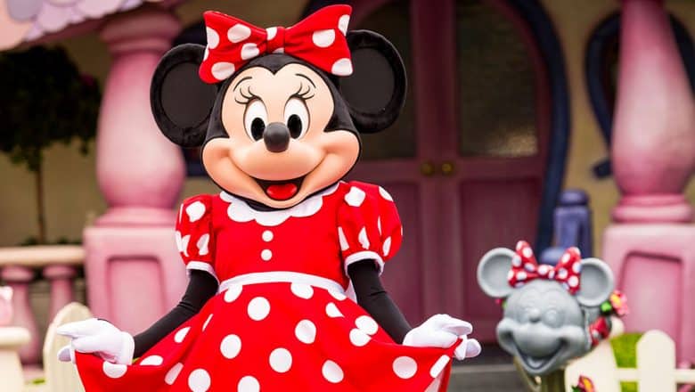 Minnie Mouse, dressed in her signature red polka-dot dress and bow, greets guests with a bright smile outside her whimsical house in Disneyland. Next to her stands a charming Minnie Mouse statue—adding an extra touch of magic and fun facts that make every tour of Minnie’s home unforgettable for fans and families alike.