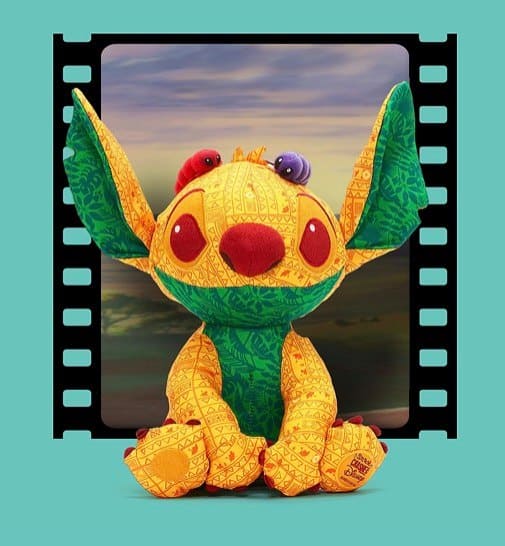 Stitch, featuring oversized ears and a Lion King-inspired makeover from the Stitch Crashes Disney Series 3 collection, sits in front of a film strip frame with a vibrant sunset backdrop, capturing the magic of Disney’s animated classics.